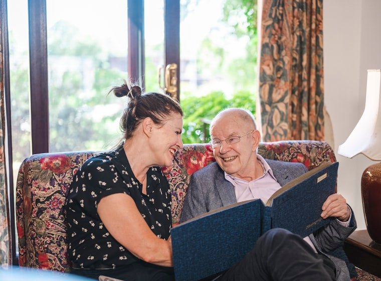 A caregiver sitting with an elderly man, looking through a book together