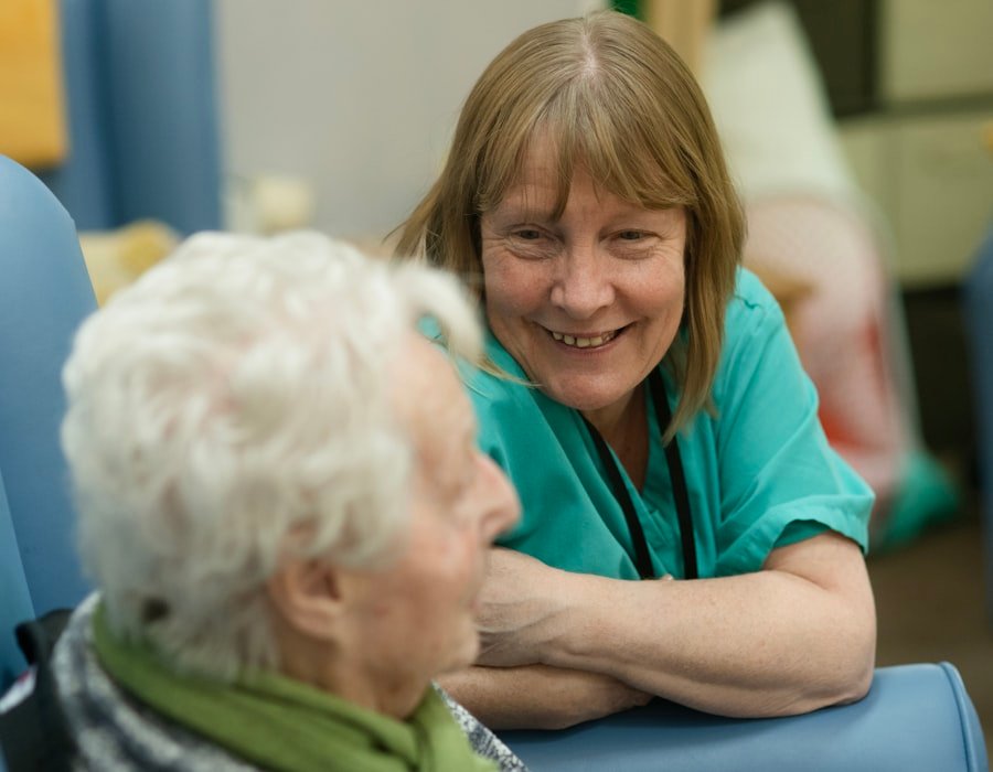 A nurse in scrubs sitting and talking with an elderly woman